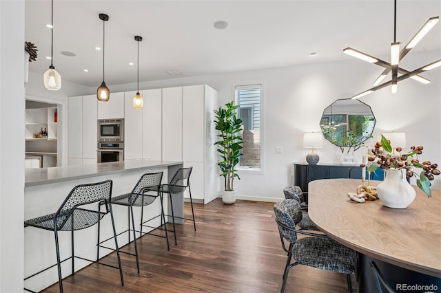 kitchen with appliances with stainless steel finishes, hanging light fixtures, dark wood finished floors, a breakfast bar, and white cabinetry