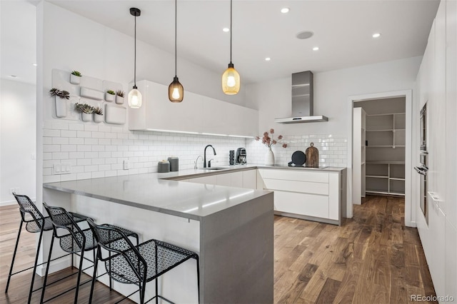 kitchen featuring backsplash, wall chimney exhaust hood, a peninsula, and wood finished floors