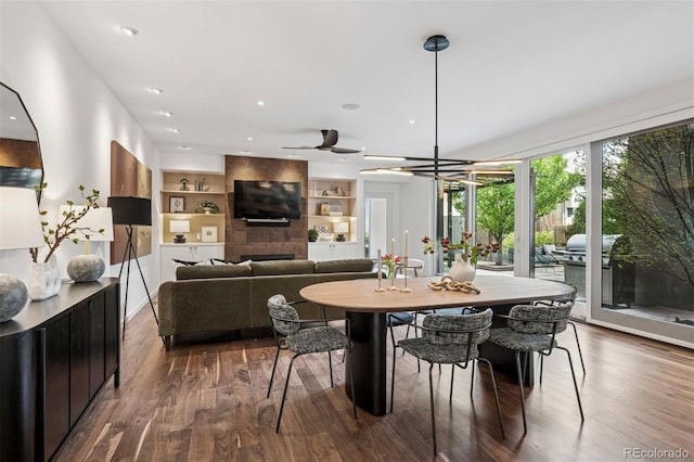 dining area with a ceiling fan, built in features, a large fireplace, wood finished floors, and recessed lighting