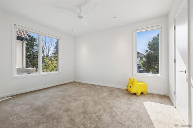 carpeted spare room with baseboards, a ceiling fan, and visible vents