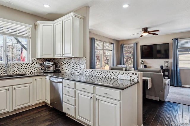 kitchen with dark countertops, dishwasher, a sink, open floor plan, and ceiling fan