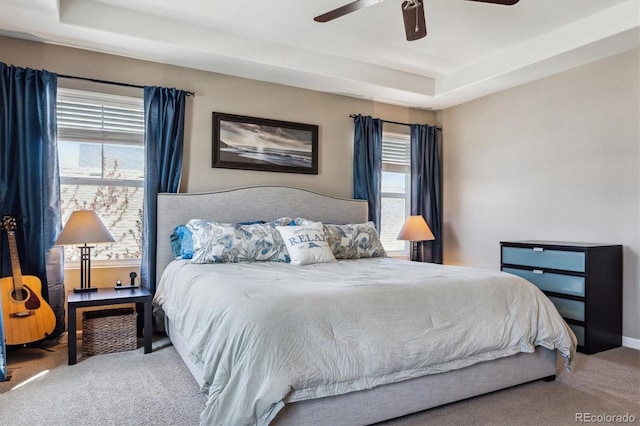 carpeted bedroom with a ceiling fan and a raised ceiling