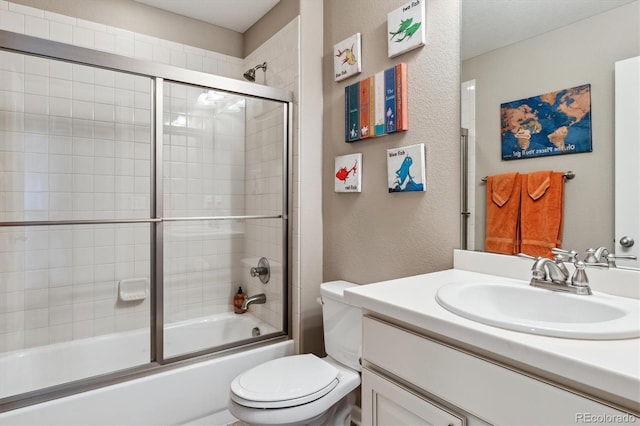 bathroom with a textured wall, vanity, bath / shower combo with glass door, and toilet