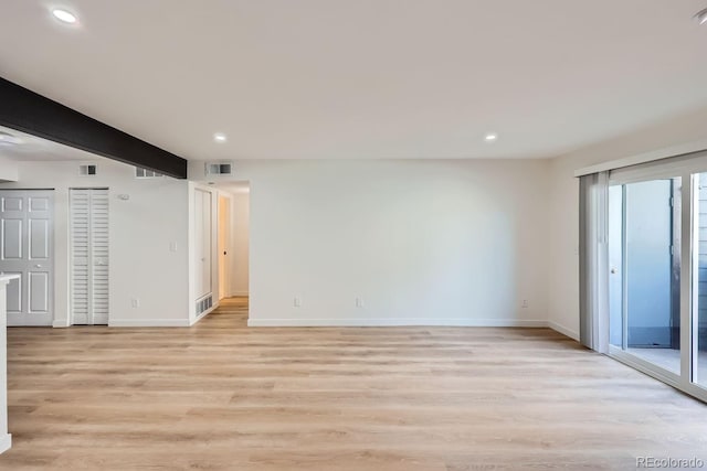 empty room featuring light wood-style flooring, beamed ceiling, visible vents, and baseboards