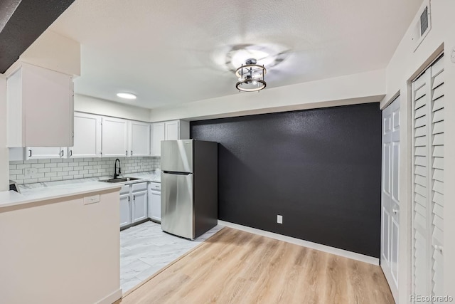 kitchen with a textured ceiling, a sink, light countertops, freestanding refrigerator, and tasteful backsplash