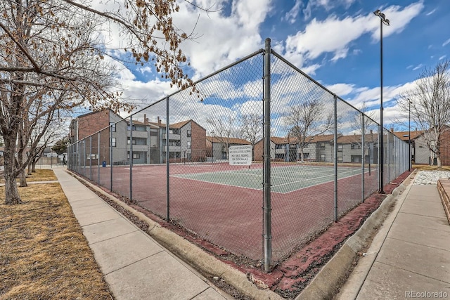 view of tennis court with a residential view and fence