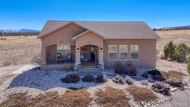 view of front of property with a shingled roof, a mountain view, covered porch, and stucco siding