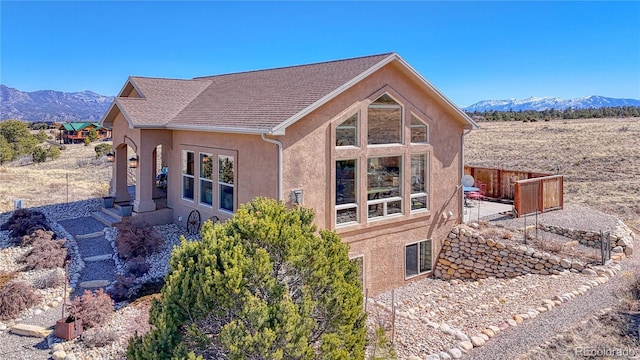 back of property featuring fence, a mountain view, roof with shingles, and stucco siding