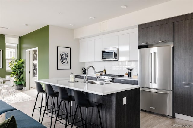 kitchen with a kitchen bar, sink, white cabinetry, a center island with sink, and high quality appliances