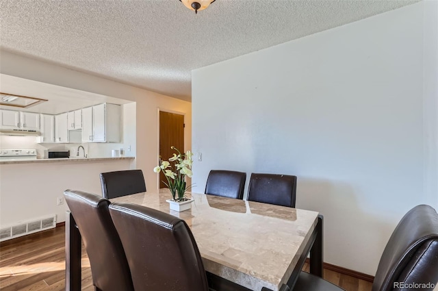 dining space featuring visible vents, baseboards, wood finished floors, and a textured ceiling