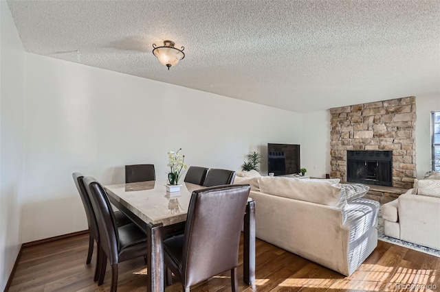dining room with a stone fireplace, wood finished floors, and a textured ceiling