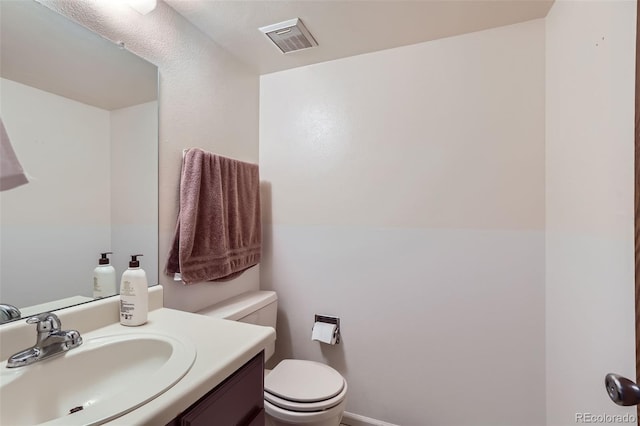 bathroom featuring toilet, vanity, and visible vents