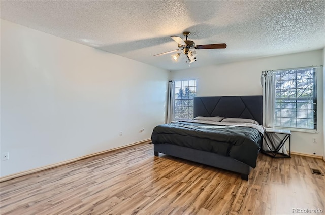 bedroom featuring baseboards, a textured ceiling, a ceiling fan, visible vents, and wood finished floors