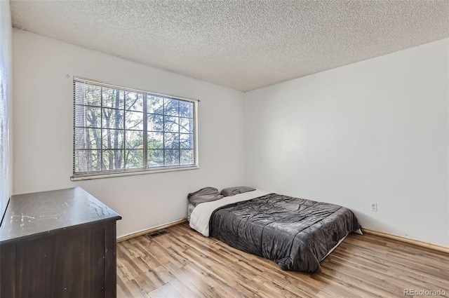 bedroom with visible vents, a textured ceiling, and wood finished floors