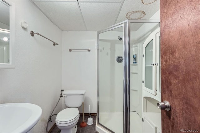 bathroom featuring a sink, toilet, a shower stall, and a drop ceiling