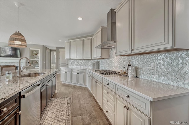 kitchen with appliances with stainless steel finishes, light stone counters, wall chimney range hood, decorative light fixtures, and sink