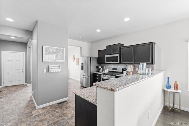 kitchen featuring light stone counters, kitchen peninsula, appliances with stainless steel finishes, and backsplash