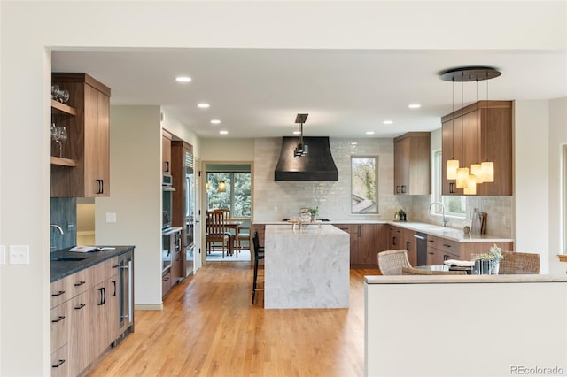 kitchen with a breakfast bar, decorative light fixtures, sink, light wood-type flooring, and wall chimney exhaust hood