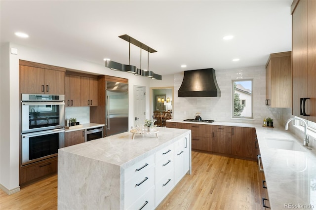 kitchen with sink, white cabinetry, a center island, appliances with stainless steel finishes, and custom range hood