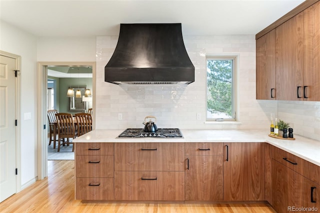 kitchen with tasteful backsplash, light wood-type flooring, stainless steel gas stovetop, and premium range hood