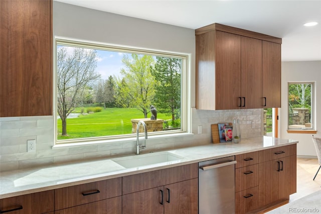 kitchen with light stone counters, sink, stainless steel dishwasher, and a healthy amount of sunlight