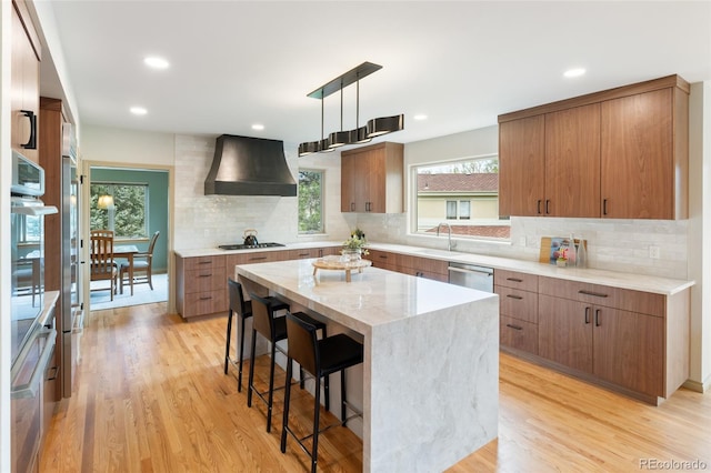 kitchen with a kitchen island, a kitchen breakfast bar, hanging light fixtures, stainless steel appliances, and custom range hood