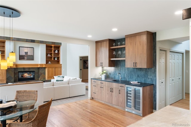 kitchen featuring a tile fireplace, sink, beverage cooler, hanging light fixtures, and light hardwood / wood-style flooring