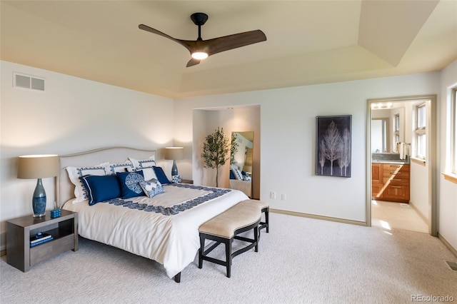 carpeted bedroom featuring a raised ceiling, ceiling fan, and ensuite bathroom