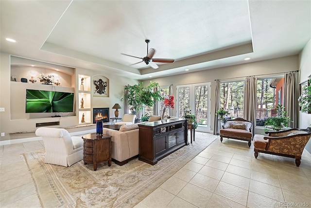 tiled living room featuring built in features, ceiling fan, a tray ceiling, and french doors