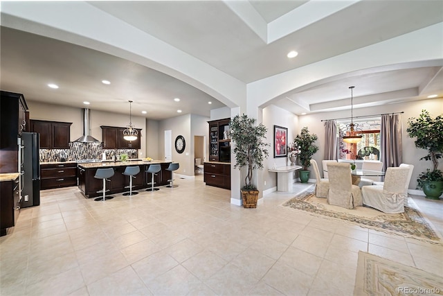 kitchen featuring decorative light fixtures, black refrigerator, tasteful backsplash, a breakfast bar area, and wall chimney range hood