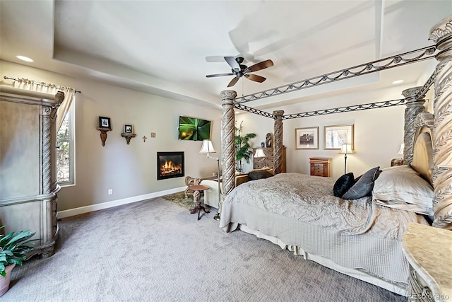 bedroom featuring ceiling fan, dark colored carpet, and a raised ceiling