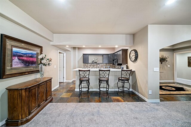 kitchen featuring dark tile floors, backsplash, a kitchen breakfast bar, and kitchen peninsula