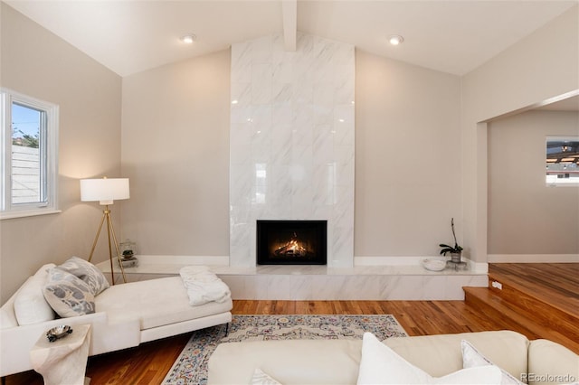 living room featuring vaulted ceiling with beams, wood finished floors, a high end fireplace, and baseboards