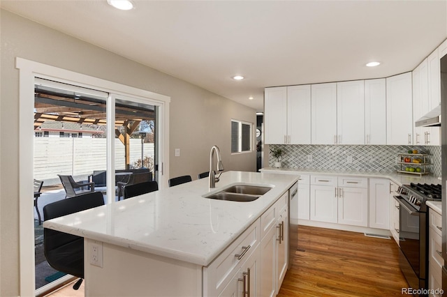 kitchen featuring tasteful backsplash, light stone counters, black gas stove, light wood-style floors, and a sink