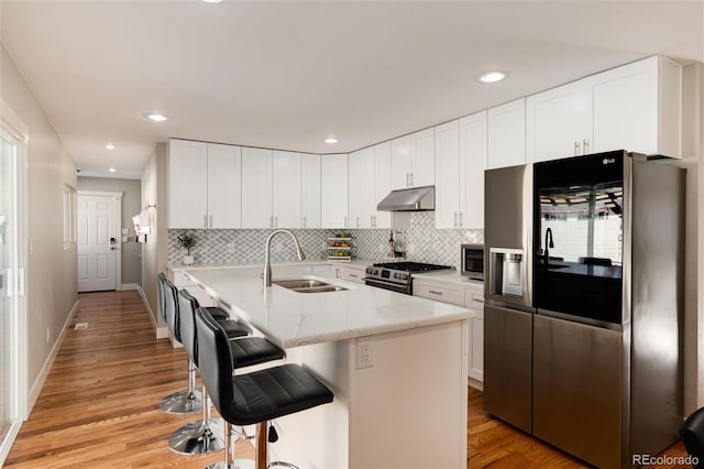 kitchen with appliances with stainless steel finishes, a sink, under cabinet range hood, and decorative backsplash