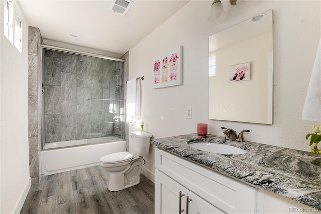 full bathroom featuring visible vents, toilet, shower / bath combination with glass door, wood finished floors, and vanity