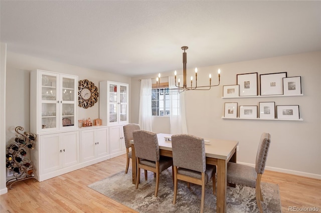 dining space with light wood-style flooring, a chandelier, and baseboards
