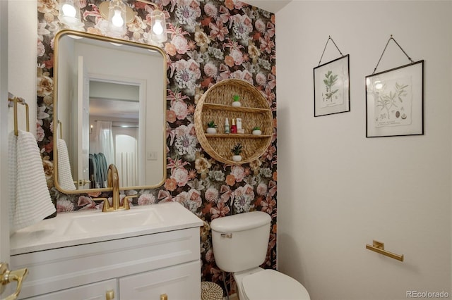 half bathroom with toilet, vanity, and wallpapered walls