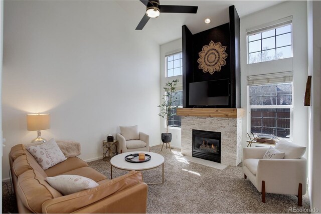 carpeted living room with plenty of natural light, a towering ceiling, a fireplace, and a ceiling fan