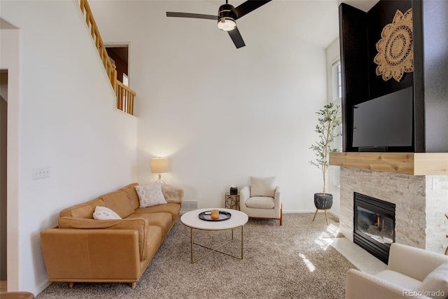carpeted living area with baseboards, ceiling fan, a towering ceiling, and a stone fireplace