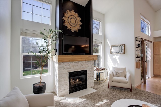 carpeted living area featuring a stone fireplace and a high ceiling