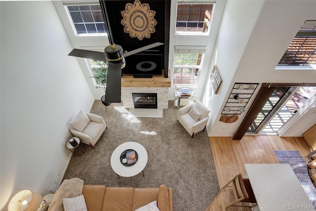 living area with a fireplace with flush hearth, wood finished floors, and a towering ceiling