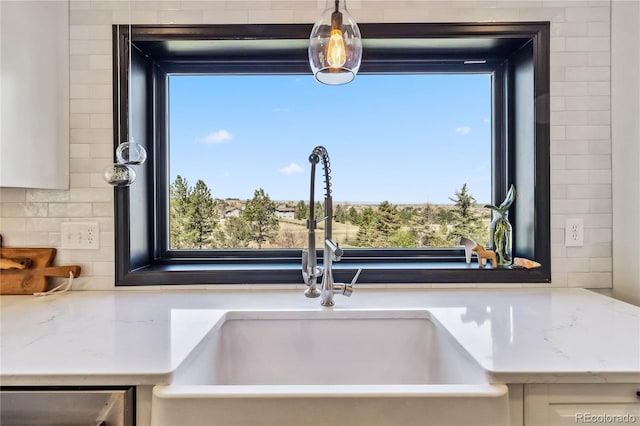 kitchen view of a sink, decorative backsplash, stainless steel dishwasher, and light stone countertops