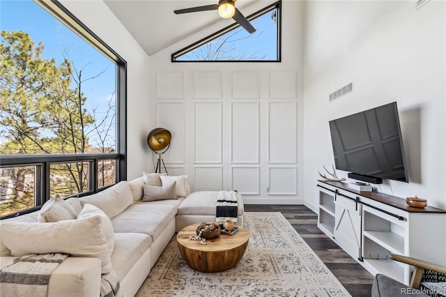 living area with ceiling fan, high vaulted ceiling, plenty of natural light, and dark wood-type flooring