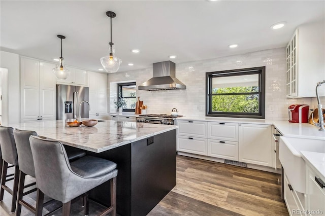 kitchen featuring wall chimney exhaust hood, high end refrigerator, a sink, decorative backsplash, and white cabinets