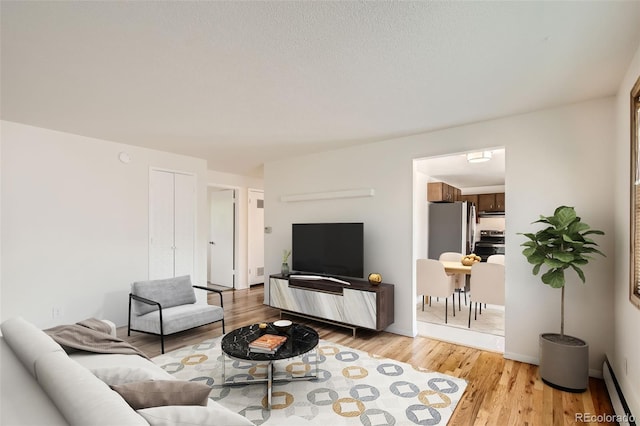 living room featuring light wood-type flooring, baseboard heating, and a textured ceiling