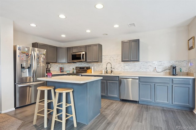 9316 Harrison St, Thornton, CO 80229 - kitchen featuring stainless steel appliances, a sink, light wood finished floors, a kitchen breakfast bar, and backsplash