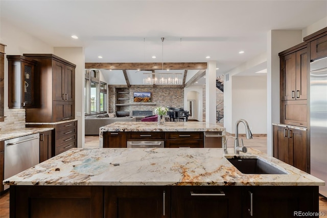 kitchen with dark brown cabinetry, a sink, a kitchen island with sink, open floor plan, and tasteful backsplash