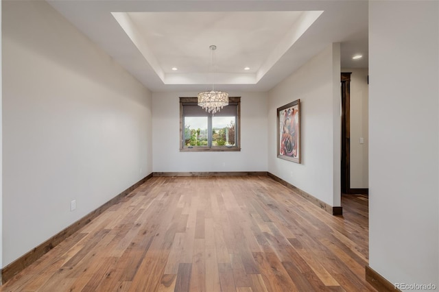 empty room featuring a chandelier, recessed lighting, baseboards, a tray ceiling, and hardwood / wood-style flooring