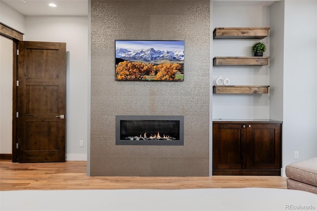 interior space with a glass covered fireplace, baseboards, recessed lighting, and wood finished floors